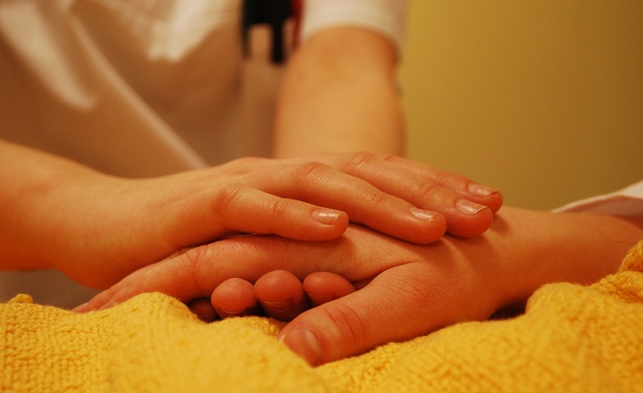 Eine Pflegerin greift die Hand eines Kranken.